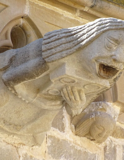 Gárgola de la Iglesia de Santa María la Mayor de Valderrobres (Teruel). Es una figura humana: una mujer con vestido abotonado y pelo largo y lacio, que sostiene un objeto en sus manos. Está en el costado meridional de la iglesia.