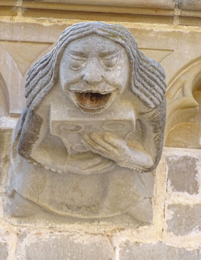 Gárgola de la Iglesia de Santa María la Mayor de Valderrobres (Teruel). Es una figura humana: una mujer con vestido abotonado y pelo largo y lacio, que sostiene un objeto en sus manos. Está en el costado meridional de la iglesia.