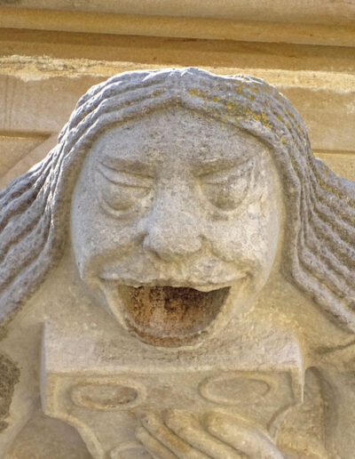 Gárgola de la Iglesia de Santa María la Mayor de Valderrobres (Teruel). Es una figura humana: una mujer con vestido abotonado y pelo largo y lacio, que sostiene un objeto en sus manos. Está en el costado meridional de la iglesia.