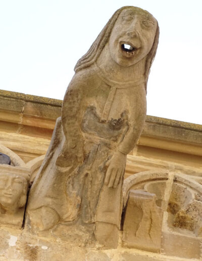 Gárgola de la Iglesia de Santa María la Mayor de Valderrobres (Teruel). Es una figura humana: una mujer con vestido con dobladillo y cinturón. Tiene el pelo largo y lacio. Está en la zona nordeste de la iglesia.